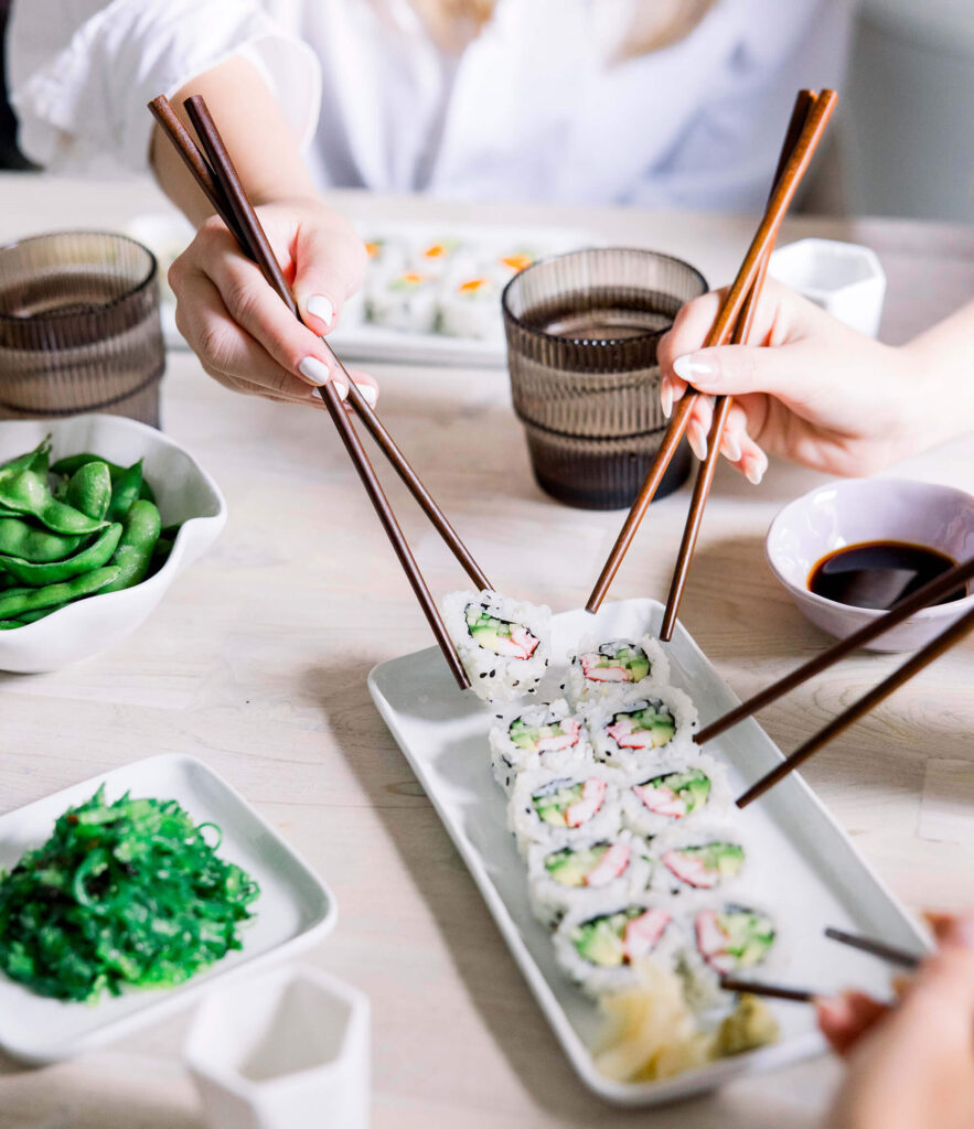 3 pairs of chopsticks grabbing sushi off of a plate